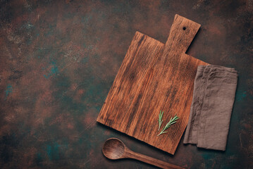 A culinary background with a wooden cutting board, wooden spoon, and linen napkin. Dark rusty grunge cooking backdrop. Top view, flat lay, copy space.