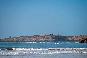 Sailboat moves quietly through the calm waters off Essaouira's coast on a clear, sunny day.