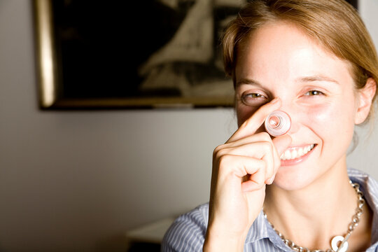 Smiling woman holding glass bottle plug playfully indoors