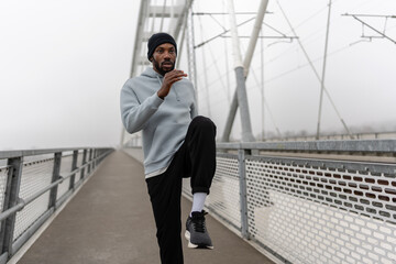 Athletic man performing high knees exercise during outdoor workout on a pedestrian bridge. Cardio training, balance and coordination drill, urban fitness lifestyle and healthy living