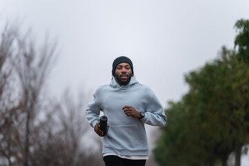 Man jogging on a red running track in a misty park, wearing a hoodie and sportswear. Outdoor fitness, healthy lifestyle, and endurance training on a foggy autumn or winter morning