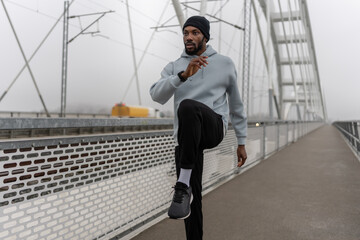 Athletic man resting in squat position during outdoor workout on a pedestrian bridge. Focused cardio training, urban fitness routine, strength and endurance exercise, active lifestyle