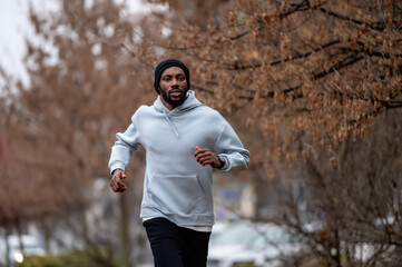 Man jogging on a red running track in a misty park, wearing a hoodie and sportswear. Outdoor fitness, healthy lifestyle, and endurance training on a foggy autumn or winter morning