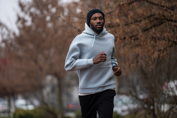 Man jogging on a red running track in a misty park, wearing a hoodie and sportswear. Outdoor fitness, healthy lifestyle, and endurance training on a foggy autumn or winter morning