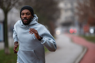 Man jogging on a red running track in a misty park, wearing a hoodie and sportswear. Outdoor fitness, healthy lifestyle, and endurance training on a foggy autumn or winter morning