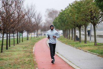 Man jogging on a red running track in a misty park, wearing a hoodie and sportswear. Outdoor fitness, healthy lifestyle, and endurance training on a foggy autumn or winter morning
