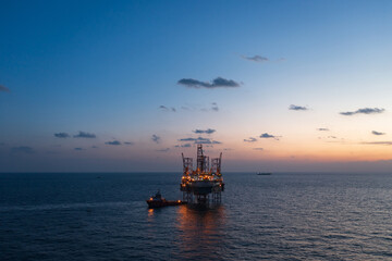 Obraz premium Aerial view from a drone of big jack up offshore drilling oil rig, production platform and supply vessel In the ocean during sunset - Oil and Gas Industry