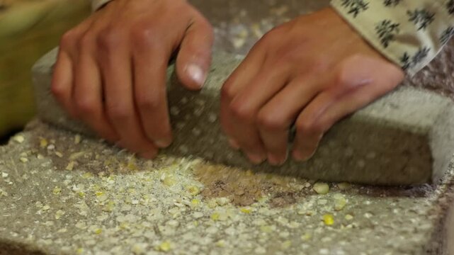 SLOW MOTION CLOSE UP SHOT OF A MAN GRINDING CORN AT A MOLCAJETE