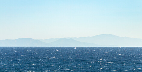 Vast blue ocean with distant mountains and sailboat  © MARINA