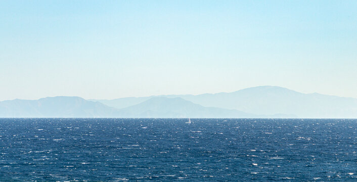 Vast blue ocean with distant mountains and sailboat
