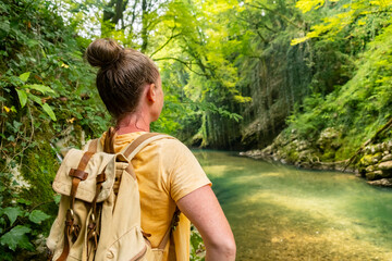 Woman explores a forest pathway alongside a clear river in daylight