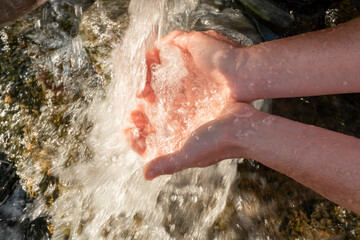 Water flows over hands in a natural setting with sunlight shining on the scene during daytime hours