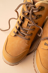 Stylish youth children's yellow men's boots made of genuine leather with laces on beige background top view. Rough-soled boots, work shoes, travel footwear close-up. Stylish nubuck shoes
