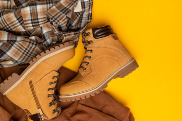 Fashionable clothes for child, boy, teenager. Yellow boots made of genuine leather nubuck, plaid shirt, brown trousers on yellow background. Rough autumn-winter work boots with ribbed sole and laces 