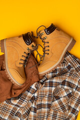 Fashionable clothes for child, boy, teenager. Yellow boots made of genuine leather nubuck, plaid shirt, brown trousers on yellow background. Rough autumn-winter work boots with ribbed sole and laces 