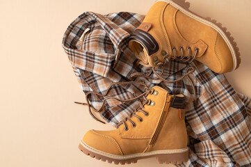 Fashionable clothes for child, boy, teenager. Yellow boots made of genuine leather nubuck, plaid shirt on beige background. Rough autumn-winter work boots with ribbed sole and laces 