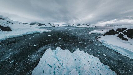 Aerial view of the frigid waters speckled with ice, contrasting with the stark, snow-covered landscapes of Paradise Bay, Antarctica.
