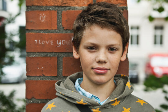 Portrait of smiling boy in hoodie standing by brick wall outdoors in Berlin