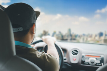 Rear view of man driving a car towards the city. Transportation, travel, and lifestyle concept with blurred cityscape.