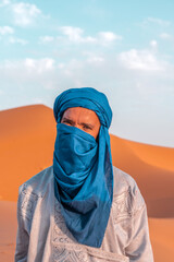 Berber man in blue turban covering face looking at camera in the Sahara desert
