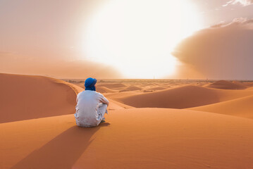 Rear view of Berber man watching sunset over sand dunes in Sahara Desert, Morocco
