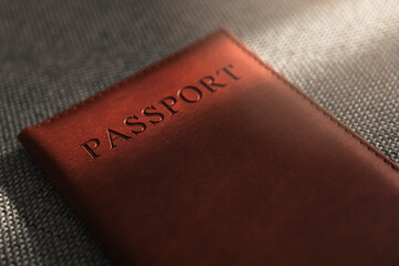 Brown leather passport cover on textured fabric in soft sunlight, minimalist travel document still life with copy space