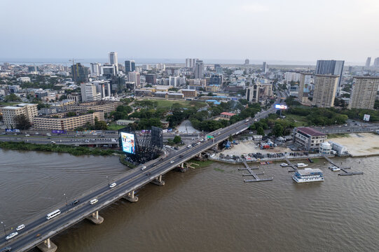 Aerial view of Falomo Bridge's concrete arches span the murky waters, connecting Victoria Island to Lagos Island under a vast, pale sky, Lagos, Lagos, Nigeria.