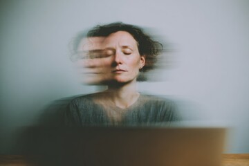person sitting at a desk with eyes closed, laptop screen reflected softly on face, neutral background, no devices visible, modern burnout concept, calm realism
