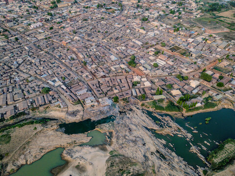 Aerial view of a vibrant urban sprawl meeting the rugged terrain and tranquil waters of Kabala Costain, Kaduna, Nigeria.