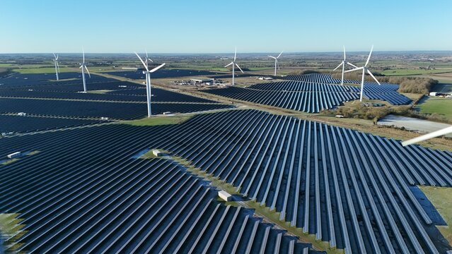 Aerial view of solar farms and wind turbines standing in stark contrast to the clear blue sky, Wellingborough, England, United Kingdom.
