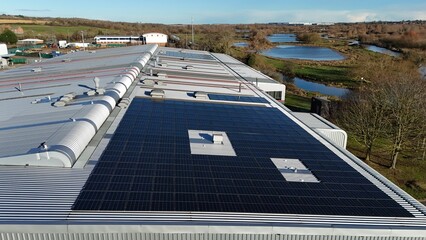 Aerial view of solar panels gleaming atop a building's roof, contrasting with the distant lakes and sparse winter trees, Wellingborough, England, United Kingdom.