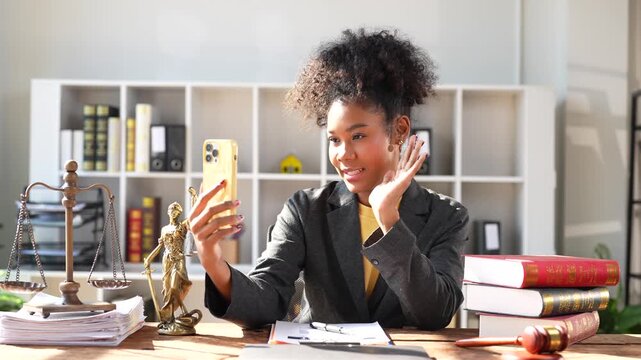 Smiling African American female lawyer sitting at her desk in a law firm office and talking on a video call, providing professional legal advice and online consultation to a client