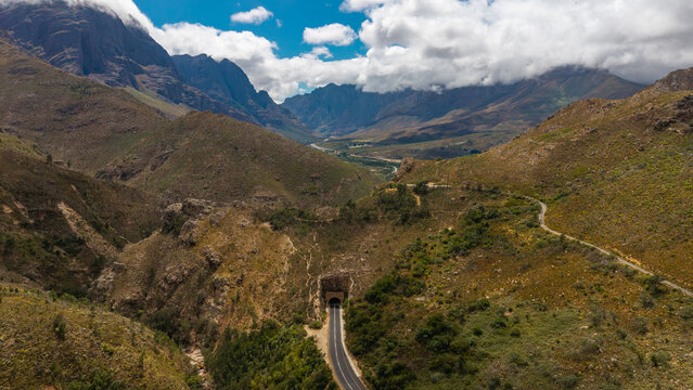 Aerial view of the Du Toitskloof Pass winding through rugged mountains, the tunnel contrasting with the green and brown landscape, Paarl, Western Cape, South Africa.