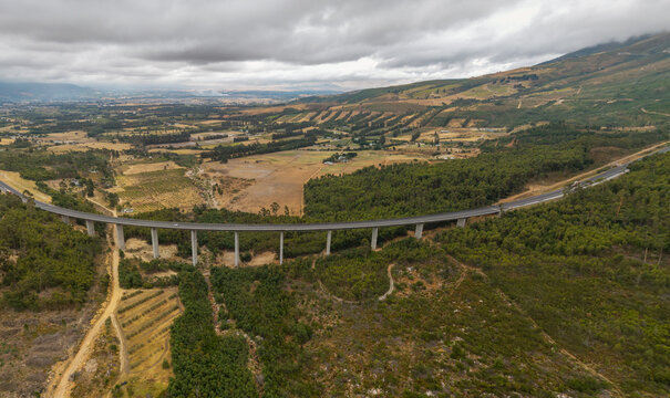 Aerial view of a modern bridge cutting through the lush green landscape, connecting the mountainous terrain against a cloudy sky, Paarl, Western Cape, South Africa.
