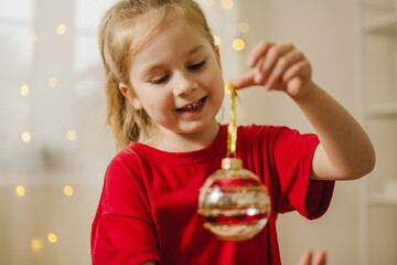 Smiling child in red pyjama decorating with Christmas ornament at home