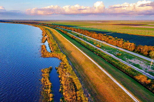 Aerial view of a tranquil lake reflecting the sky next to a grassy levee that separates the water from distant green fields, Florida, United States.