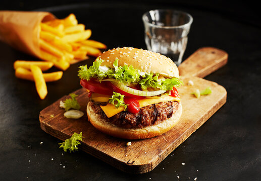 Cheeseburger with lettuce tomato onion and fries on wooden board