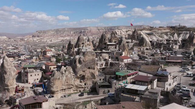 Aerial drone footage of G&ouml;reme town in Cappadocia, Turkey, surrounded by fairy chimneys and volcanic rock formations. The shot reveals traditional stone houses, cave dwellings carved into soft tuff ro