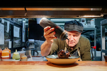 Chef plating gourmet chocolate ice cream dessert in restaurant kitchen