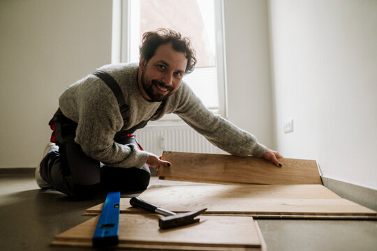 Smiling adult installing laminate flooring during home renovation