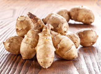 Fototapeta premium Freshly harvested Jerusalem artichoke (sunchoke) tubers with a yellow flower and green leaves, arranged on a rustic wooden table.