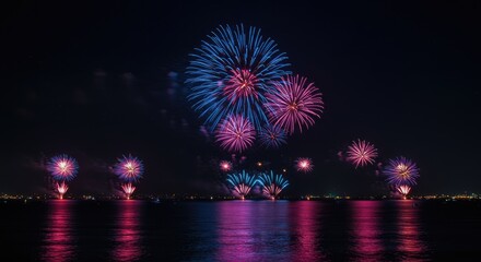 A nighttime scene of colorful fireworks exploding over a body of water, reflecting vibrant hues of pink, blue, and purple