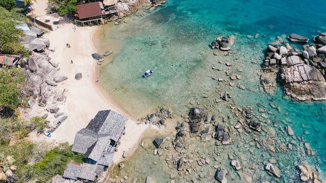Aerial view of the beach meeting the turquoise sea, with rocky outcrops and buildings nestled among lush greenery, Ko Tao, Surat Thani, Thailand.