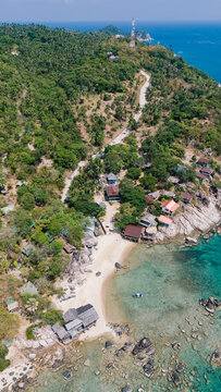 Aerial view of a tranquil bay where turquoise waters meet the sandy shore, framed by lush greenery and scattered buildings, Ko Tao, Surat Thani, Thailand.