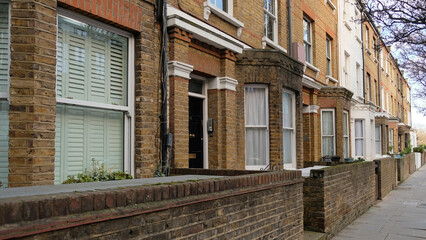 Fototapeta premium Typical Victorian terraced houses in England. Exterior view of cozy residential buildings in London with brick fence, several floors, windows and front door with molding. Real estate, Living apartment