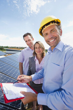 Smiling engineer and team inspecting solar panels outdoors