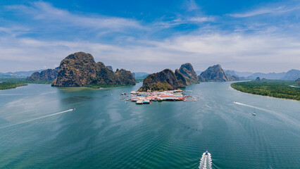 Aerial view of emerald waters embrace towering limestone karsts and a stilted village, a symphony of nature and human harmony, Phang Nga Bay, Thailand.