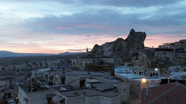 Aerial drone footage of U&ccedil;hisar village in Cappadocia, Turkey, dominated by the iconic U&ccedil;hisar Castle rising above stone houses and cave dwellings. The scene captures the town built into volcanic rock