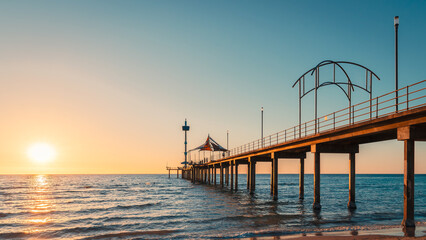 Brighton Jetty framed by the beach at sunset, with people strolling along the pier as warm evening light reflects over the ocean, South Australia.
