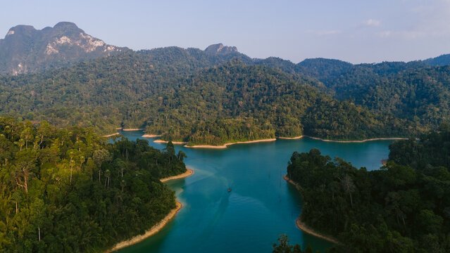 Aerial view of vibrant turquoise waters winding through the dense green canopy of Khao Sok National Park's lush rainforest, Surat Thani, Thailand.